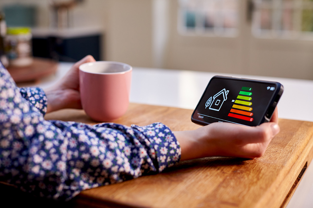 Person holding a coffee mug and a smart energy display showing the home's energy rating